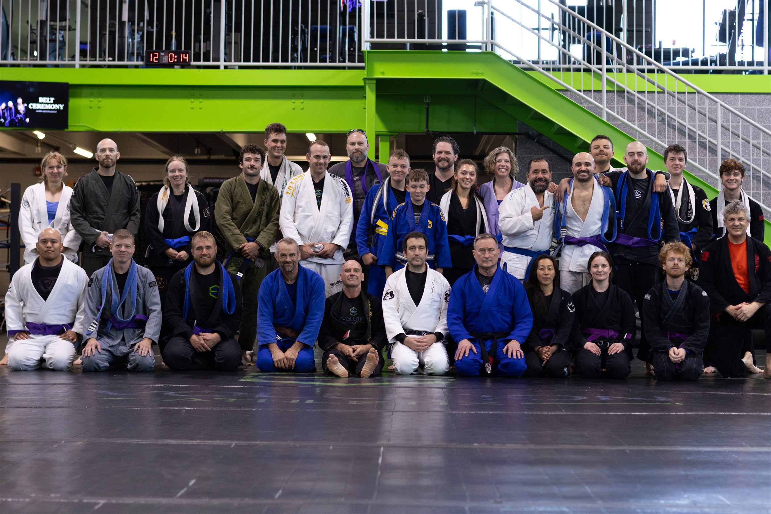 Full Evolution Athletix Brazilian Jiu Jitsu team posing in front of the green staircase after the belt promotion ceremony