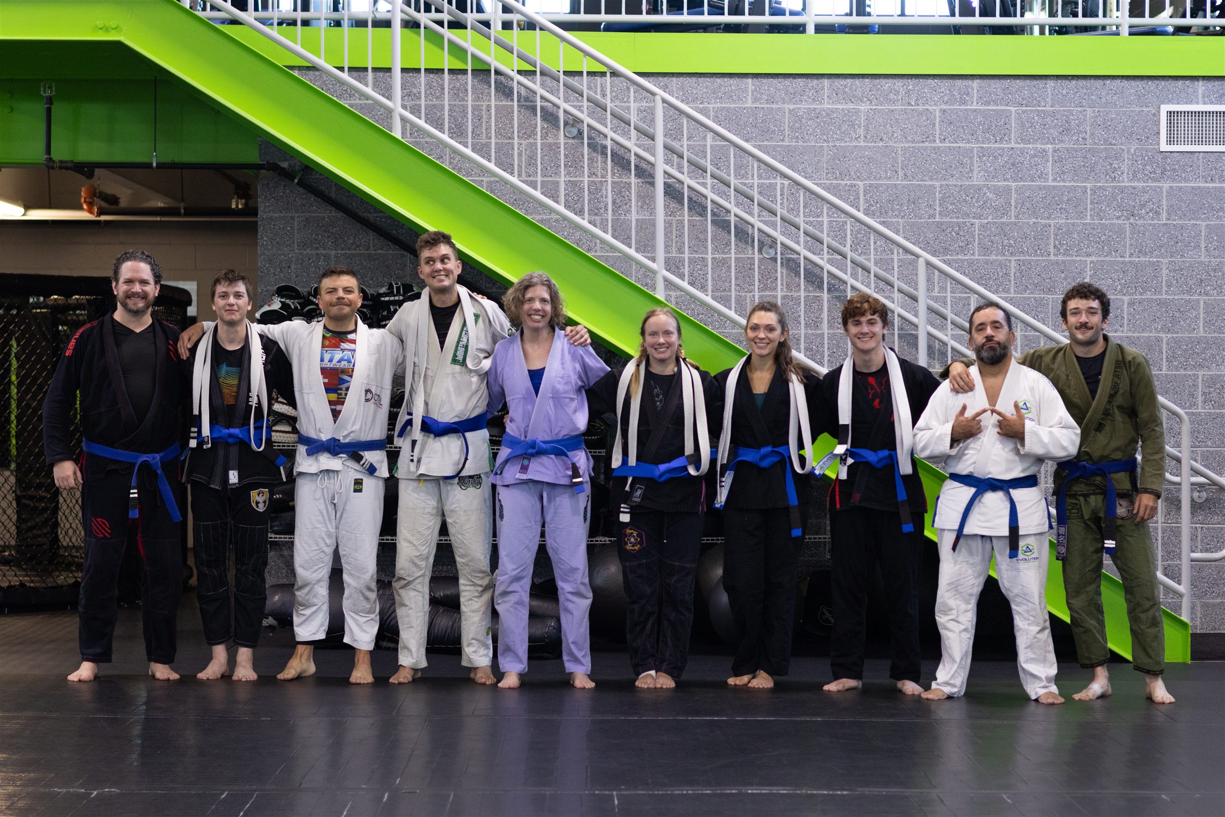 Nine Evolution Athletix Brazilian Jiu Jitsu students lined up with their new blue belts after the promotion ceremony