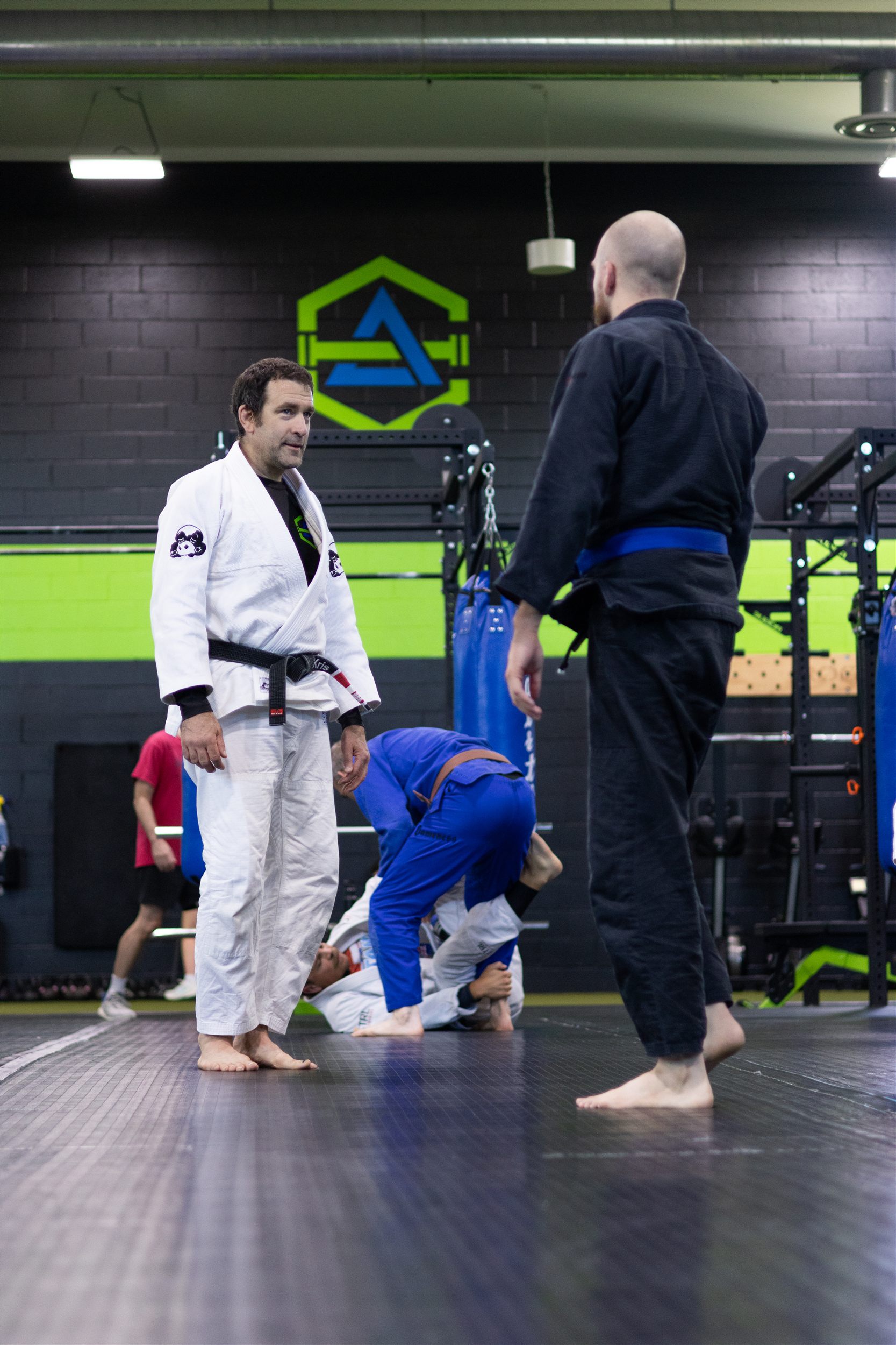 Kris Kramer, Brazilian Jiu Jitsu black belt at Evolution Athletix, giving feedback to a blue belt student in front of the gym logo